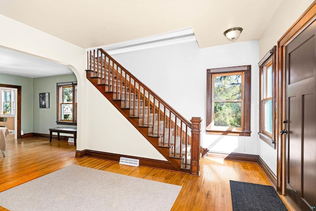 entrance foyer featuring visible vents, baseboards, stairway, hardwood / wood-style floors, and arched walkways