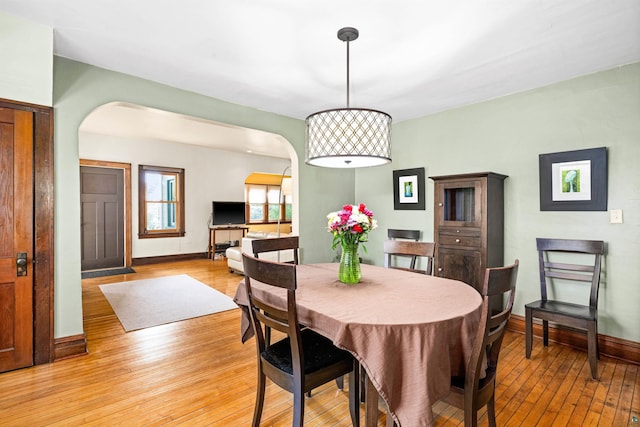 dining room with baseboards, arched walkways, and light wood-style flooring