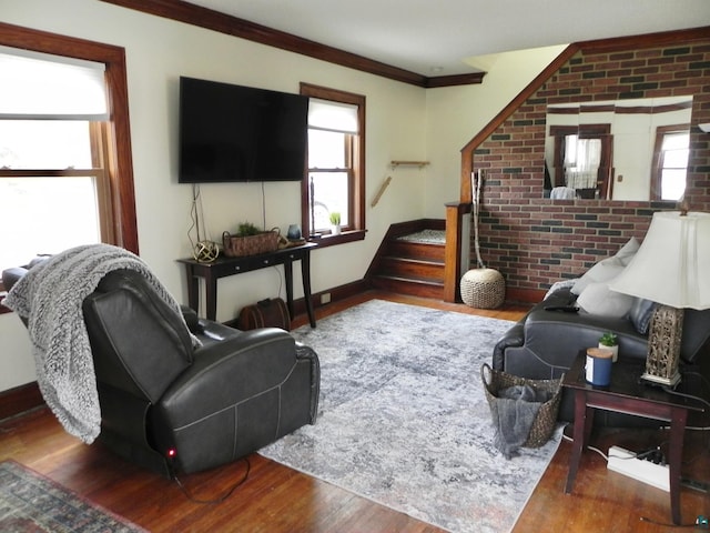 living room with ornamental molding, wood finished floors, brick wall, baseboards, and stairs