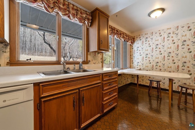 kitchen with brown cabinets, a sink, wallpapered walls, white dishwasher, and light countertops