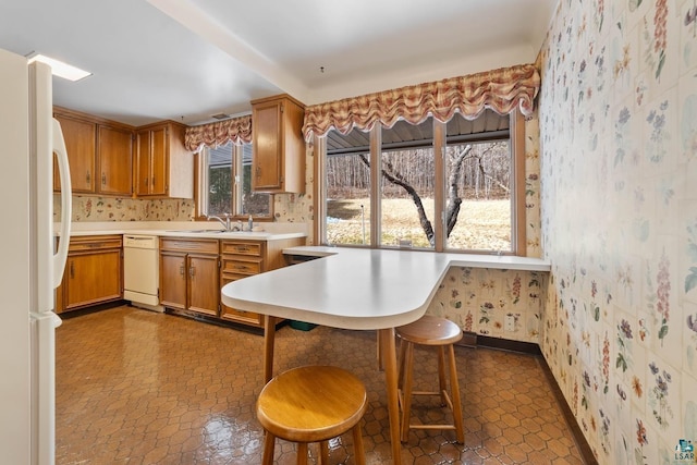 kitchen with a sink, white appliances, a breakfast bar area, brown cabinetry, and light countertops