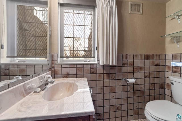 half bathroom with a wealth of natural light, visible vents, toilet, and tile walls