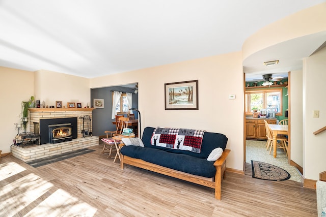 living area with a brick fireplace, baseboards, ceiling fan, and wood finished floors