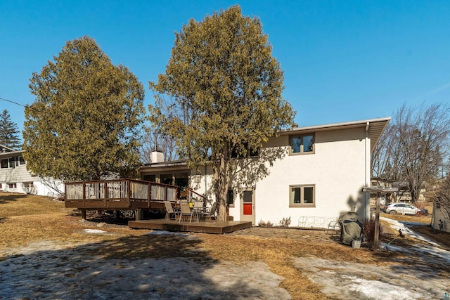 back of house with a wooden deck, a chimney, and stucco siding