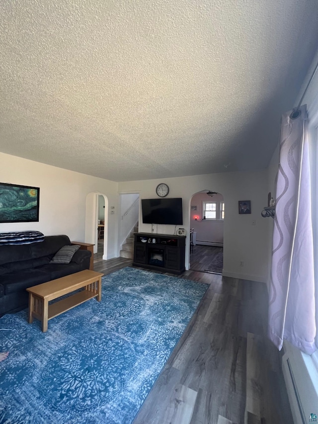 living room featuring stairway, wood finished floors, arched walkways, a textured ceiling, and a baseboard radiator