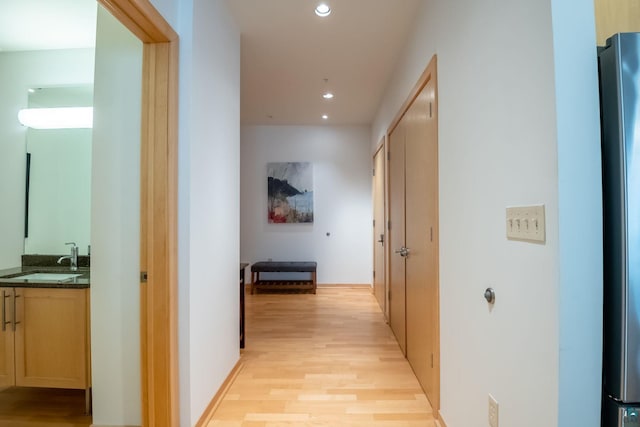 hallway featuring recessed lighting, baseboards, light wood finished floors, and a sink