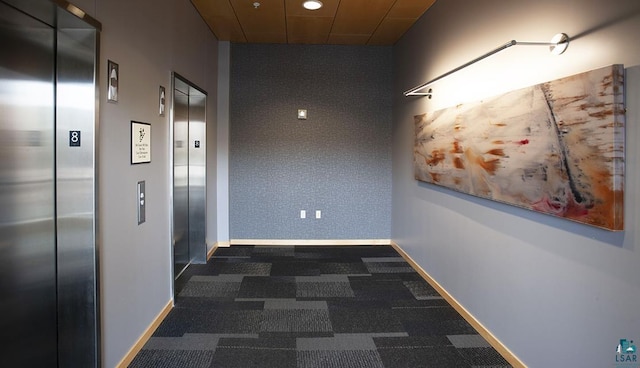 hall with baseboards, elevator, and dark carpet