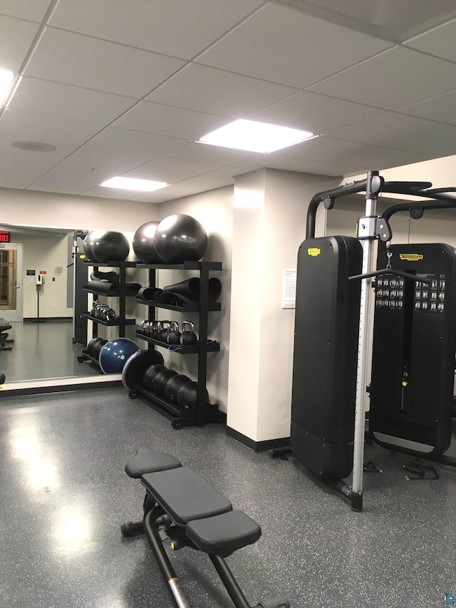 gym with a paneled ceiling and baseboards