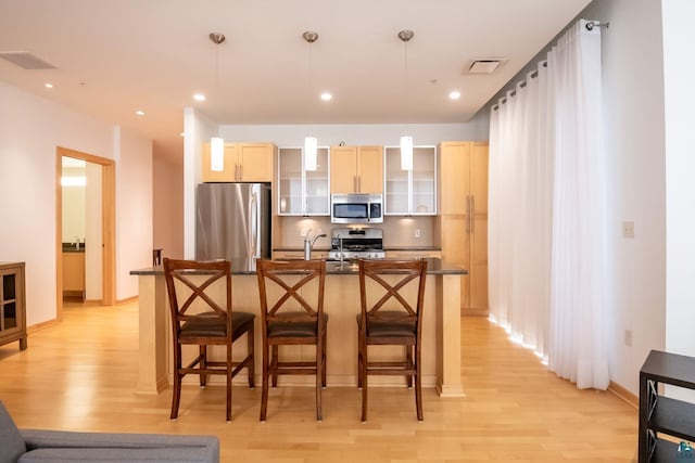 kitchen featuring dark countertops, visible vents, light wood finished floors, a breakfast bar, and appliances with stainless steel finishes