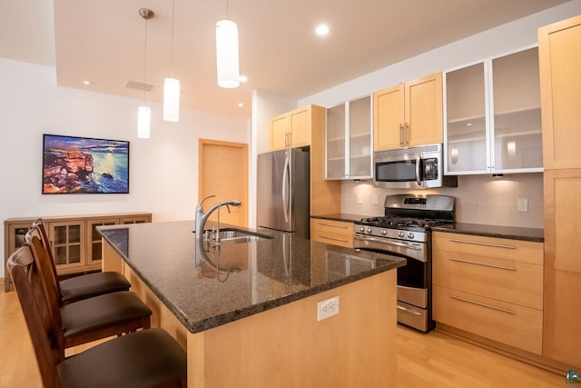 kitchen featuring a sink, a kitchen bar, appliances with stainless steel finishes, light wood-style floors, and a kitchen island with sink