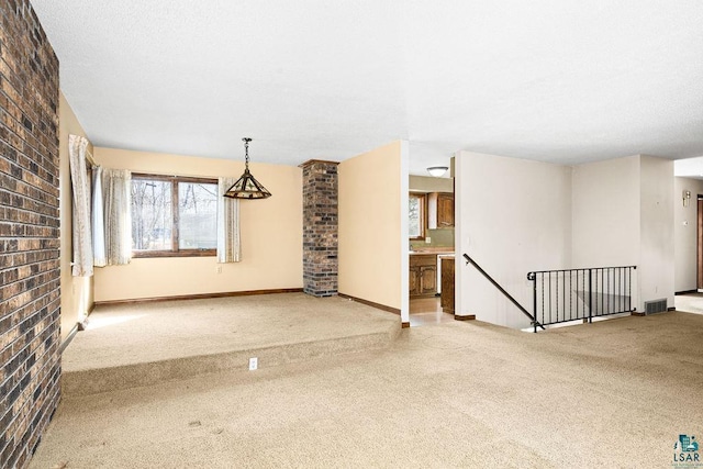 empty room with carpet, visible vents, brick wall, baseboards, and a textured ceiling