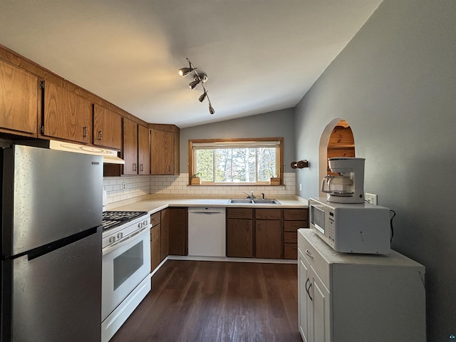 kitchen featuring white appliances, brown cabinetry, lofted ceiling, dark wood-type flooring, and backsplash