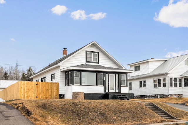 bungalow-style home with fence, roof with shingles, and a chimney