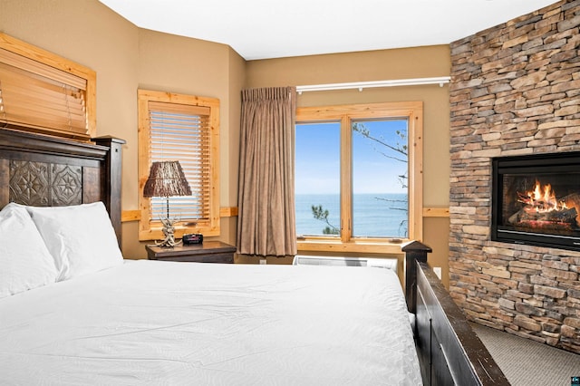 bedroom featuring multiple windows, a stone fireplace, and a water view