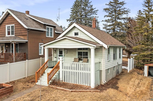 bungalow-style house featuring a porch, fence, roof with shingles, and a chimney