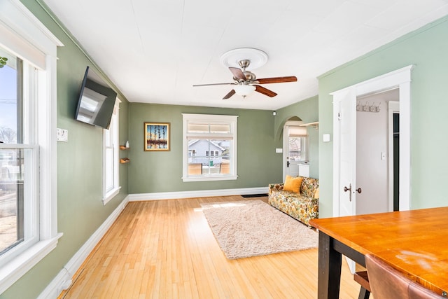 living area with arched walkways, wood finished floors, baseboards, and ceiling fan