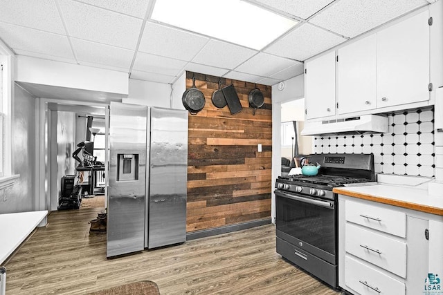 kitchen with under cabinet range hood, wood finished floors, stainless steel appliances, white cabinets, and a paneled ceiling