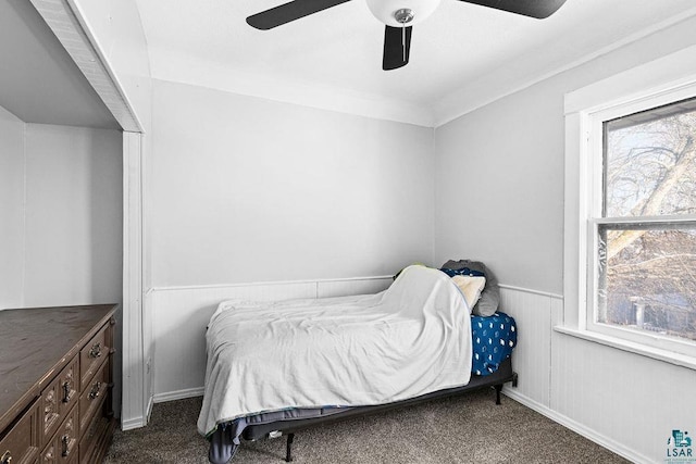 bedroom with wainscoting, dark carpet, and ceiling fan