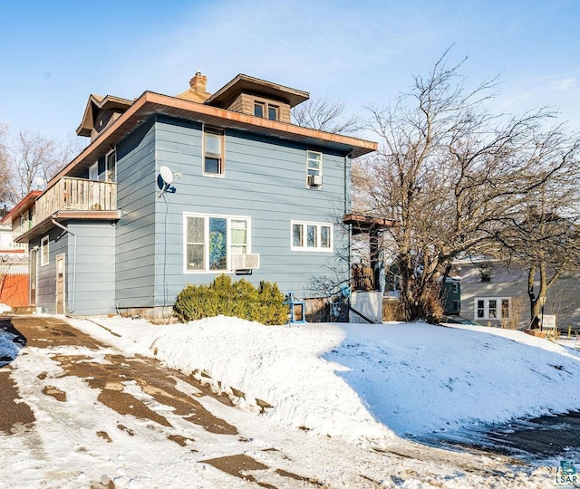 snow covered property with a balcony and a chimney