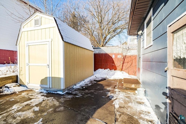 snow covered structure with an outbuilding, a shed, and fence