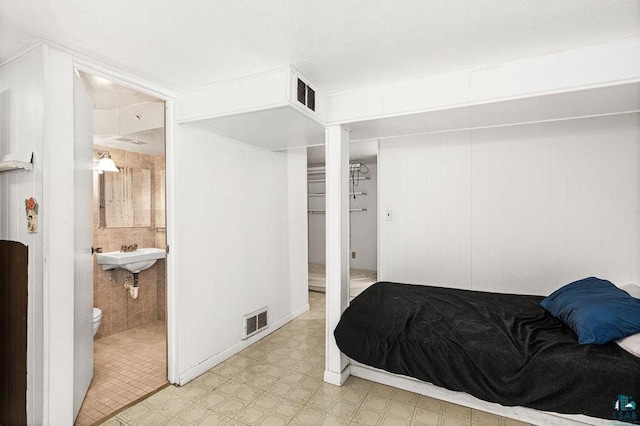 bedroom featuring a sink, visible vents, light floors, and a textured ceiling