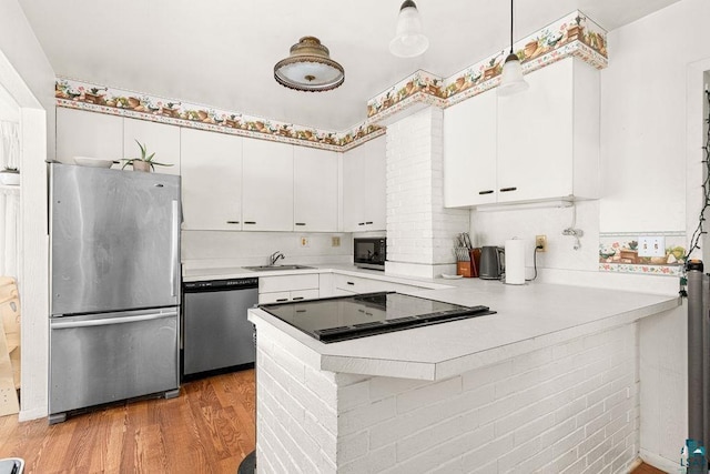 kitchen featuring ornate columns, a peninsula, stainless steel appliances, light countertops, and light wood-type flooring