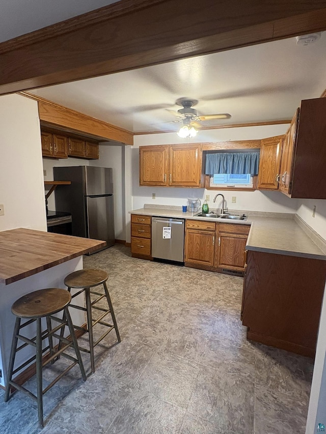 kitchen featuring a kitchen bar, brown cabinetry, stainless steel appliances, a ceiling fan, and a sink