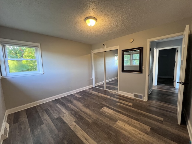 unfurnished bedroom featuring baseboards, visible vents, dark wood finished floors, a closet, and a textured ceiling