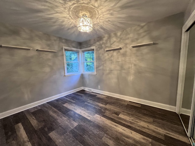 unfurnished bedroom featuring a closet, baseboards, a notable chandelier, and dark wood-style floors