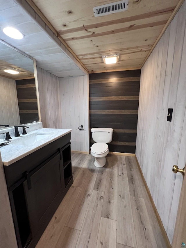 half bath with vanity, visible vents, wood-type flooring, wooden ceiling, and toilet