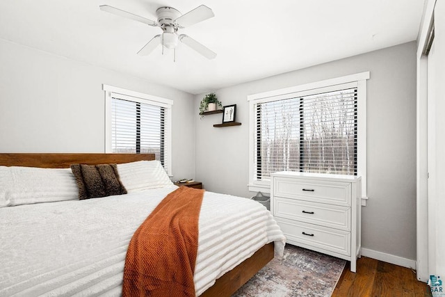 bedroom featuring dark wood finished floors, multiple windows, baseboards, and ceiling fan