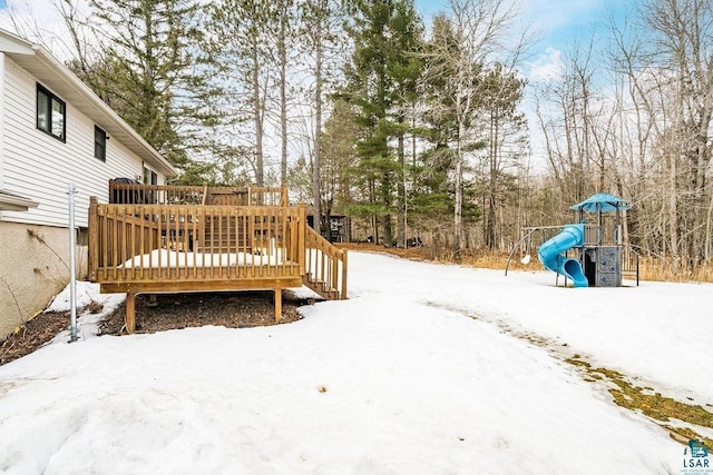 yard layered in snow with a wooden deck and a playground