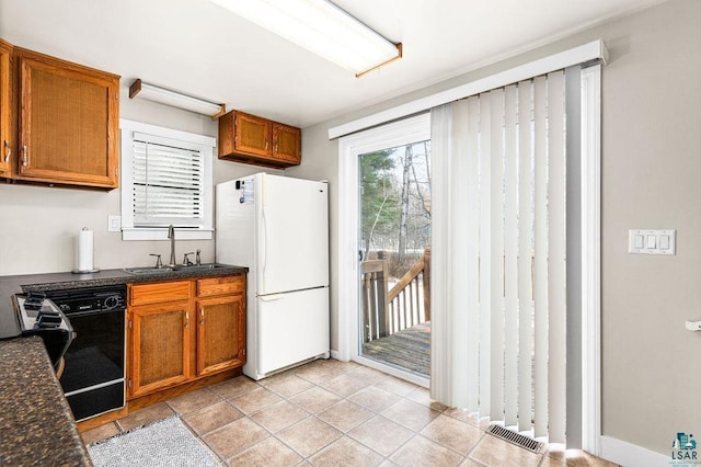 kitchen featuring a sink, black dishwasher, dark countertops, freestanding refrigerator, and brown cabinetry