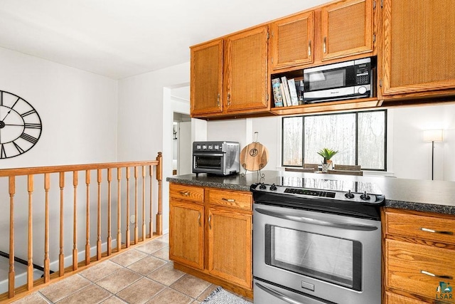 kitchen featuring dark countertops, a toaster, light tile patterned floors, brown cabinets, and appliances with stainless steel finishes