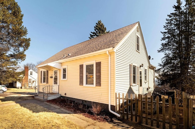 view of front facade with crawl space, a shingled roof, and fence