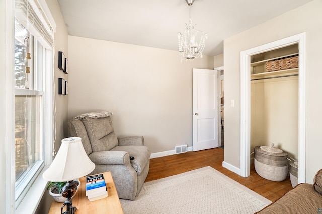 living area featuring an inviting chandelier, wood finished floors, visible vents, and baseboards