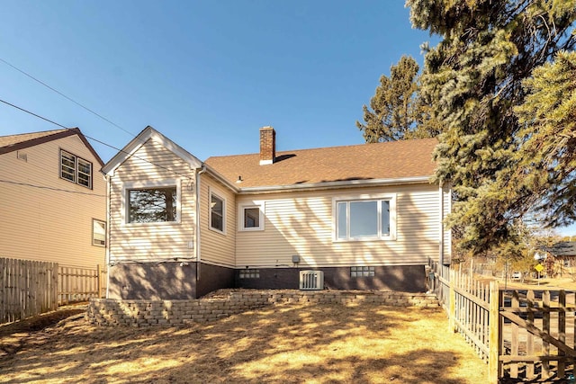 back of house featuring cooling unit, a shingled roof, a chimney, and fence