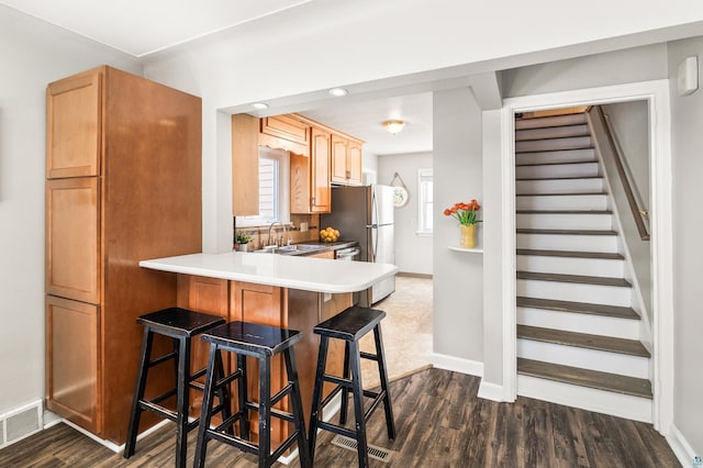 kitchen featuring a breakfast bar, dark wood-style floors, visible vents, and a sink