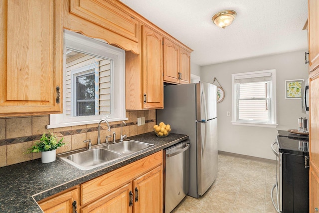 kitchen with a sink, dark countertops, backsplash, appliances with stainless steel finishes, and baseboards