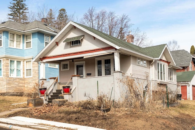 view of front of home with a porch, stone siding, and a chimney