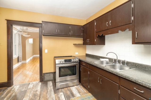 kitchen with stainless steel electric range, a sink, dark brown cabinets, light wood-style floors, and backsplash