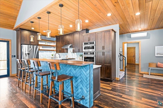 kitchen with an island with sink, dark brown cabinets, appliances with stainless steel finishes, under cabinet range hood, and tasteful backsplash