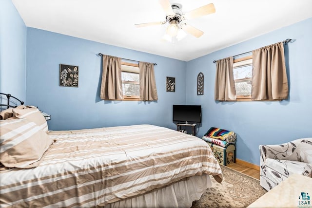 bedroom featuring a ceiling fan, multiple windows, wood finished floors, and baseboards