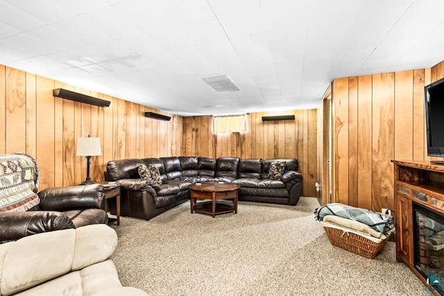 living room featuring a glass covered fireplace, wooden walls, visible vents, and carpet floors