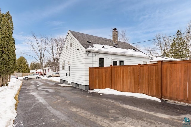 snow covered property with a chimney, roof with shingles, and fence