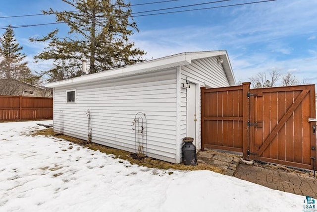 snow covered structure with an outbuilding, a gate, and fence