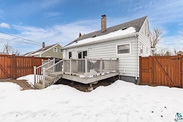 snow covered property with a chimney, fence, a deck, and a gate