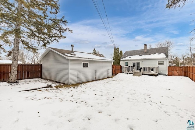 snow covered back of property with a fenced backyard and a deck