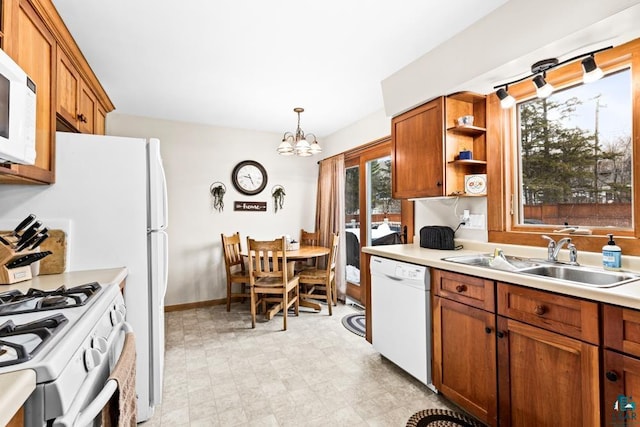 kitchen with white appliances, brown cabinetry, a sink, light countertops, and a chandelier