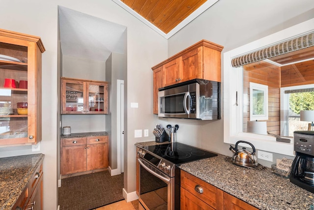 kitchen featuring brown cabinets, stainless steel appliances, dark stone counters, and vaulted ceiling